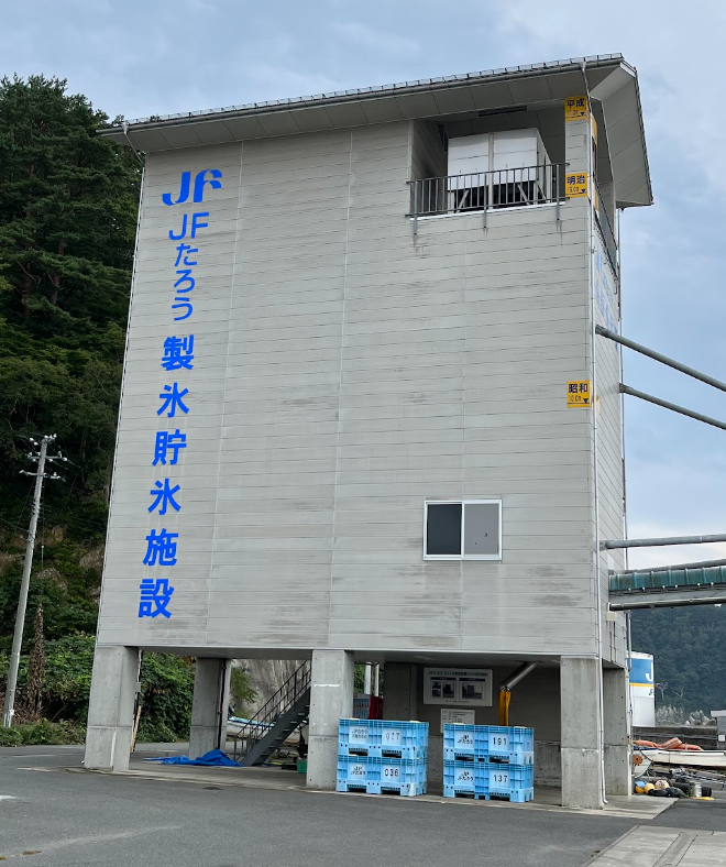 重建后的日本渔业协会田老制冰储水设施。在图片右侧可以看到3个黄色的指示牌，从下到上依次表示着1933年昭和三陆地震、1896年明知三陆地震和3·11大地震引发的海啸到达此处时的高度。